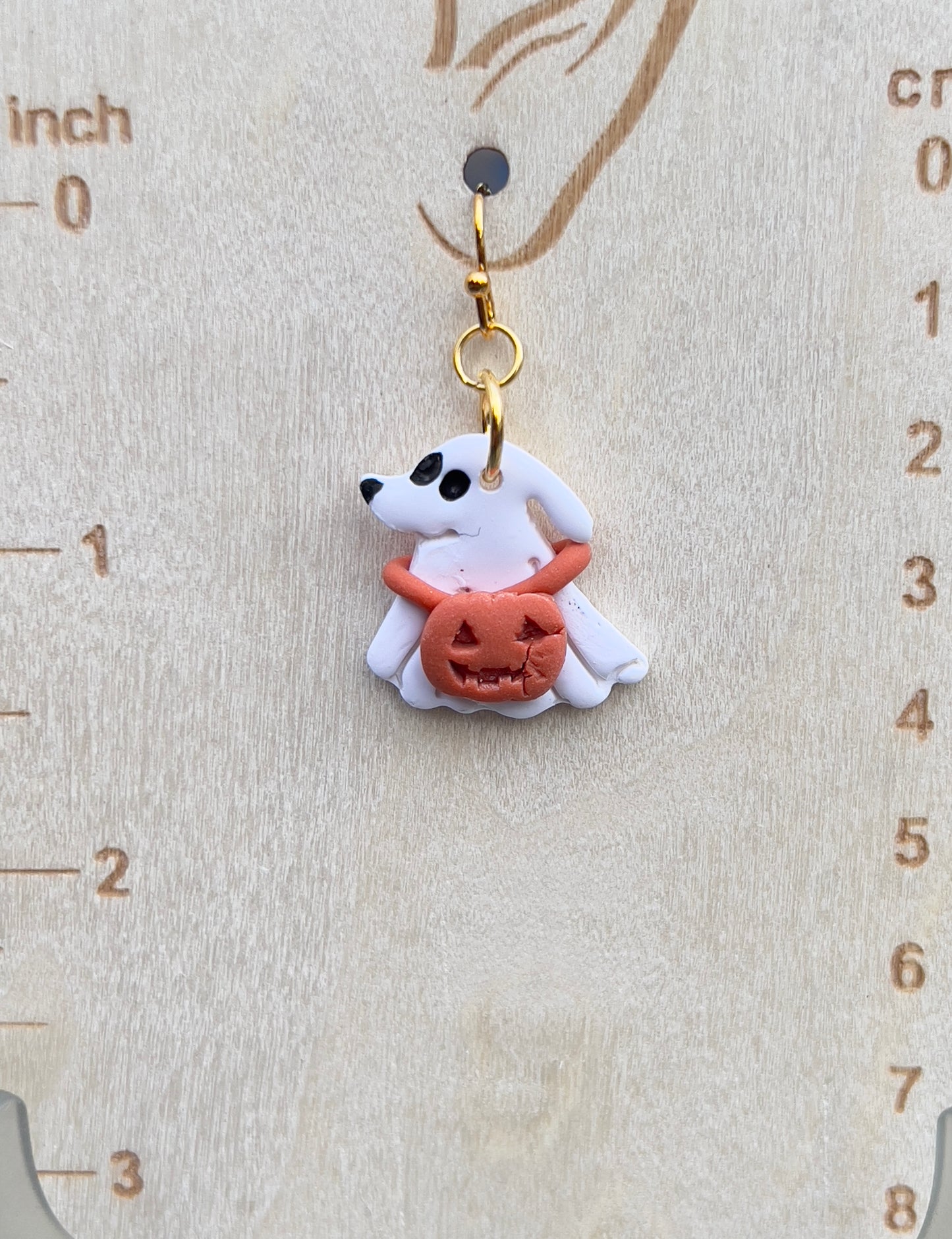 Dog Ghost with a jack-o’-lantern around its neck dangling clay earrings.